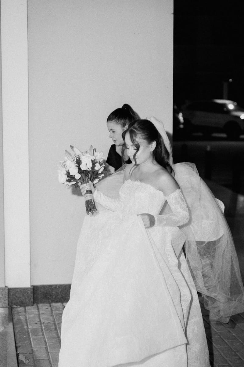 Fotografia em preto e branco de Weiri Borges ajudando a noiva com o vestido.