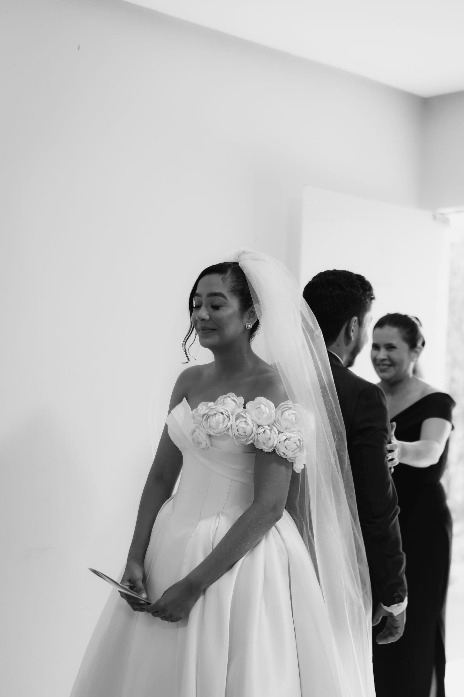 Fotografia em preto e branco da noiva com o noivo e Weiri Borges ao fundo.